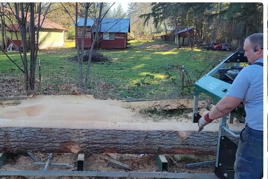 Operator milling a Douglas fir log on a green Woodland Mills HM126 portable sawmill