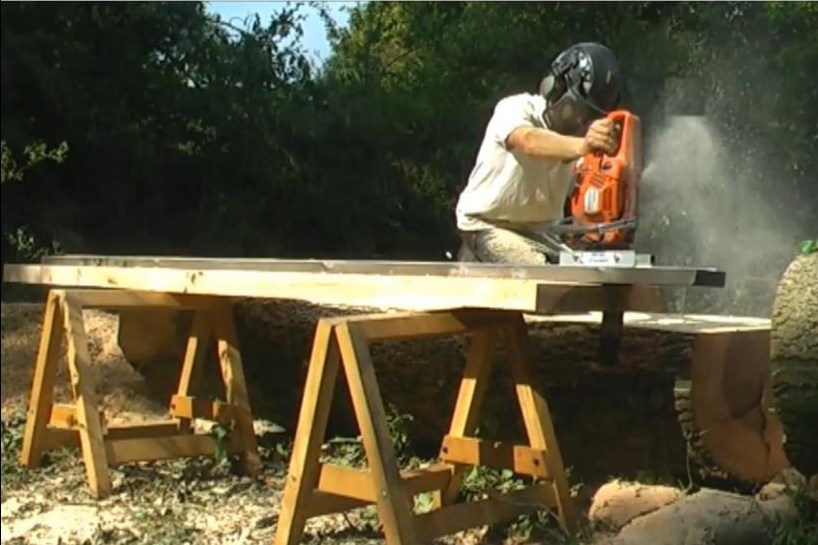 A hobbyist milling a slab in a backyard with a budget Alaskan chainsaw mill, the bar cutting horizontally across the log