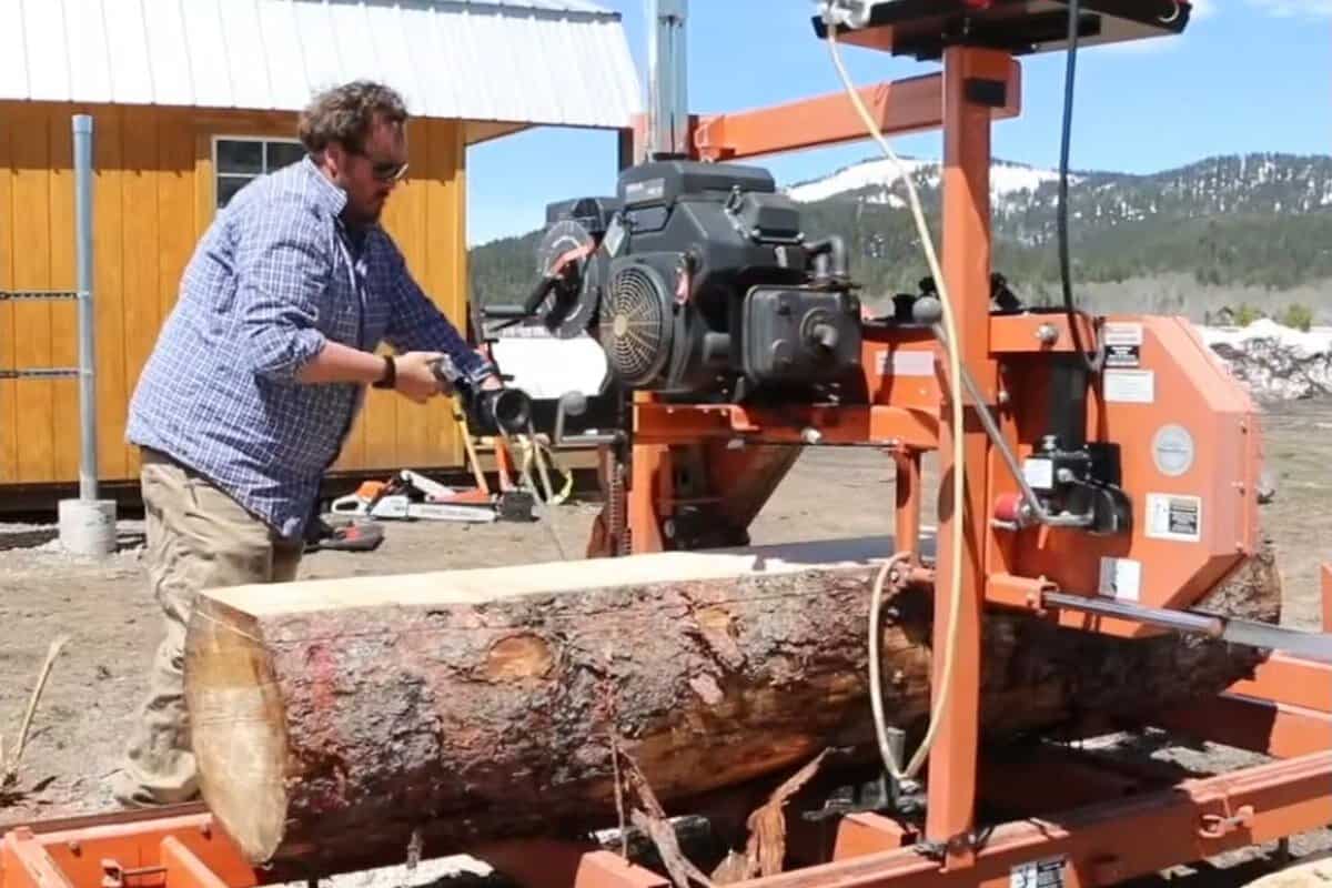 Operator pushing the sawhead of a Wood-Mizer LT15 down a log mid-cut, with the freshly sawn face visible on the near end