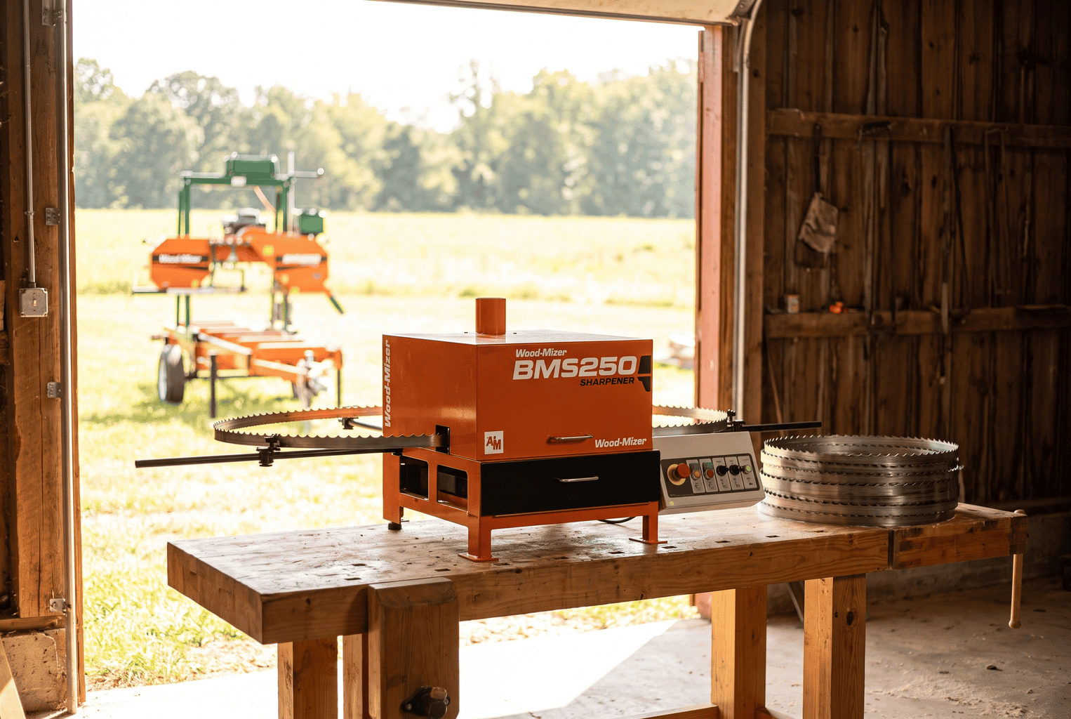 Bandsaw mill blade sharpener on a workbench in a sawmill shop doorway with a coiled sharpened blade and a portable sawmill outside